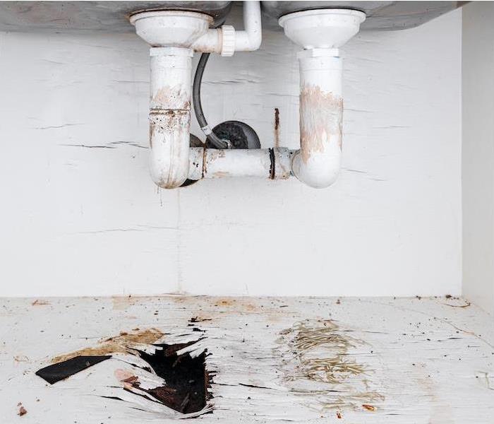 the underside of a sink showing water damage from leaking pipes